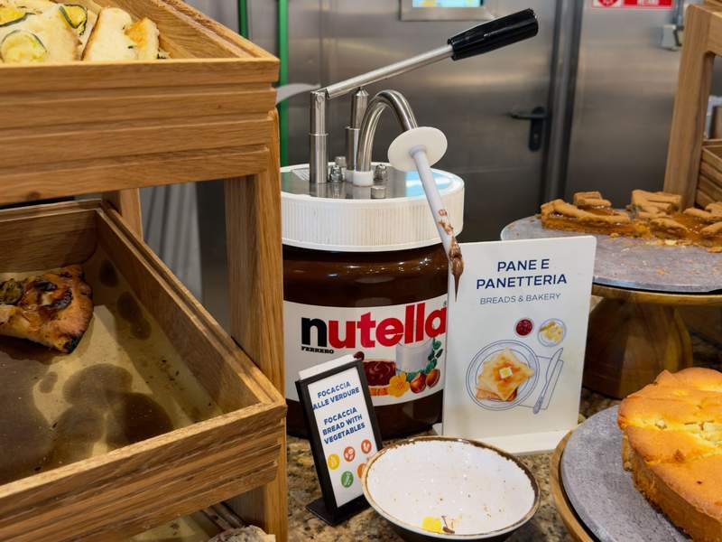 Large Nutella dispenser surrounded by focaccia, cakes and other baked goods on the Hilton Milan breakfast buffet.