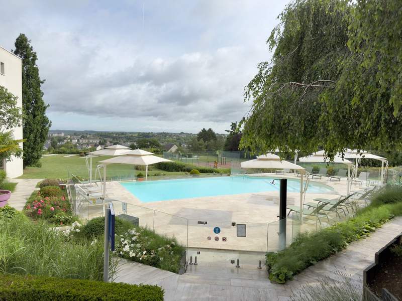 Outdoor hotel pool with white umbrellas and lounge chairs overlooking green lawns and a town with a château on the horizon