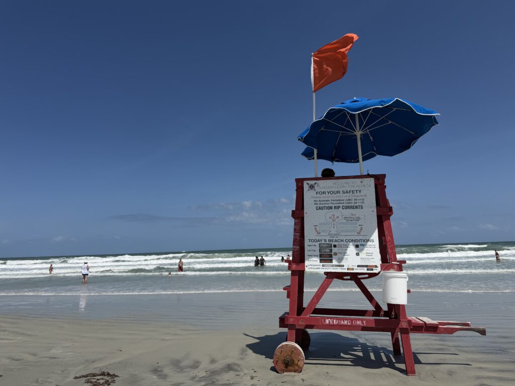 Lifeguard chair with navy umbrella and red chair on windy Atlantic Ocean beach in New Smyrna Beach.