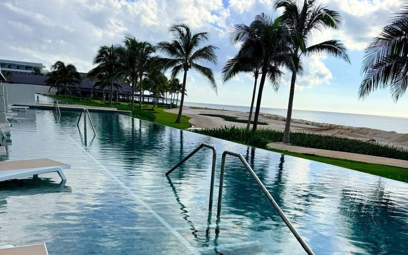 Infinity-edge swim-out pool beside the Caribbean Sea, framed by palm trees and tropical landscaping at a luxury Jamaica resort.