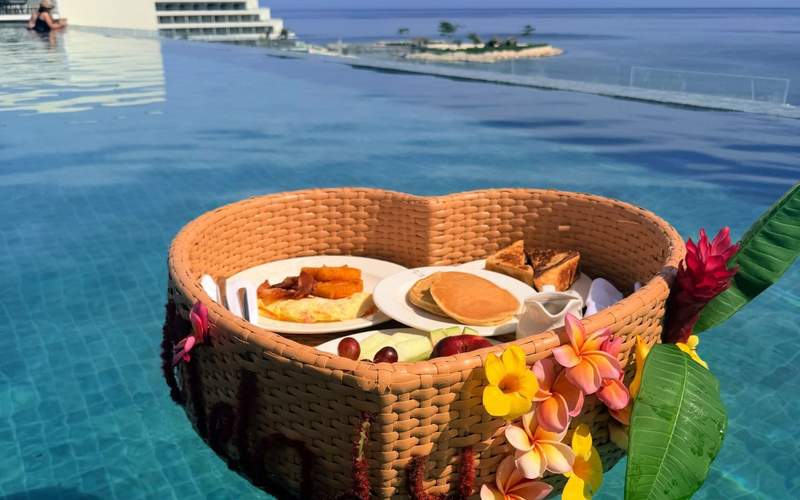 Floating breakfast in an infinity pool at Princess Senses The Mangrove featuring tropical flowers, fresh fruit, pancakes, and Caribbean Sea views.