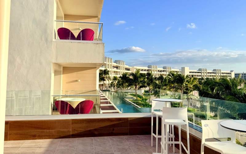Private waterfront balcony at Princess Grand Jamaica overlooking palm trees, resort pools and the Caribbean Sea.