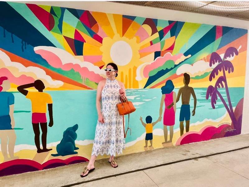 A woman posing in front of a colorful mural of a beach sunset