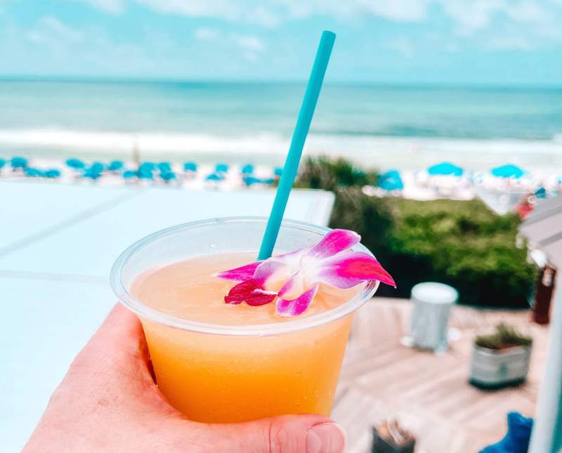A hand holding a margarita overlooking a beautiful view of a beach with turquoise water