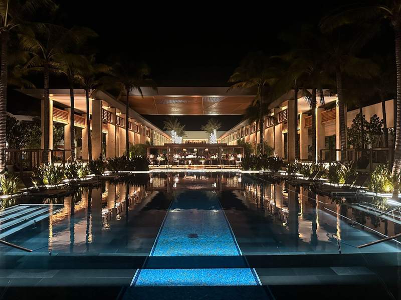 Main pool at Conrad Tulum Riviera Maya in Mexico illuminated at night, framed by palm trees and reflecting the resort’s warm lights