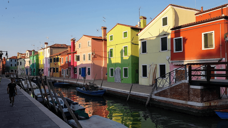 A row of brightly colored houses with a canal and boats in front of them 