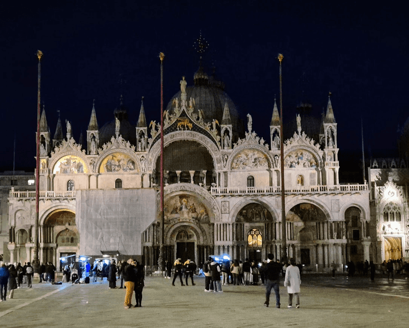 A night time photo of St. Mark's Square and St. Mark's Basilica in Venice, an ornate Byzantine-style church. 