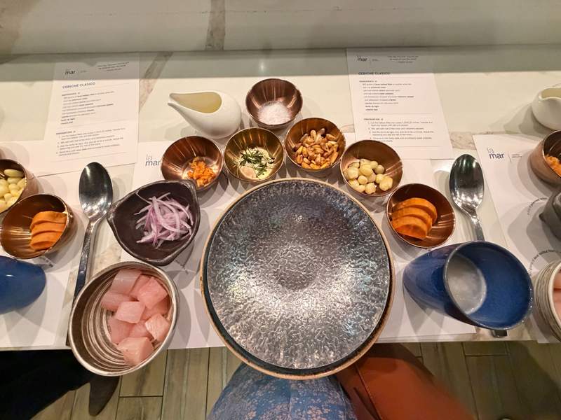 A silver bow in the center is surrounded by small bowls filled with ingredients for a cooking class. Menus and instructions are on the counter.