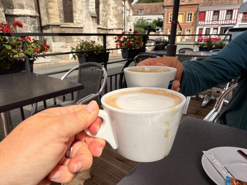 Two people toast with coffee cups in a sidewalk cafe.