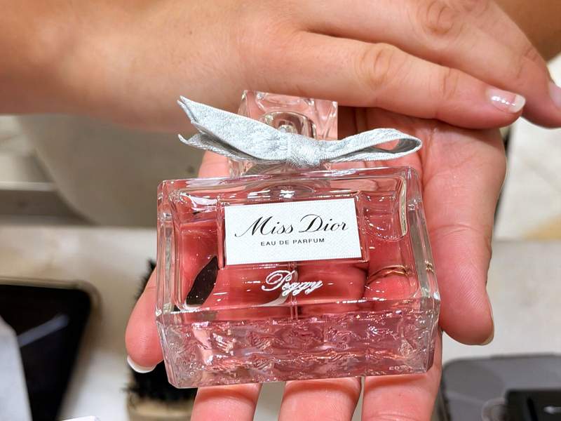 Two hands presenting a bottle of Miss Dior Eau De Parfum with its iconic pink color.