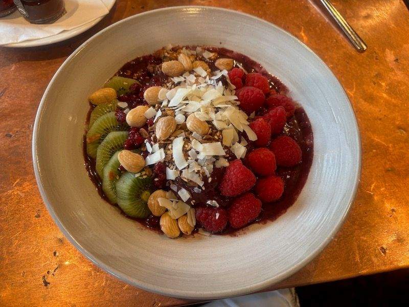 An açaí bowl served in a light-colored bowl, topped with sliced kiwi, fresh raspberries, almonds, coconut flakes, and granola.