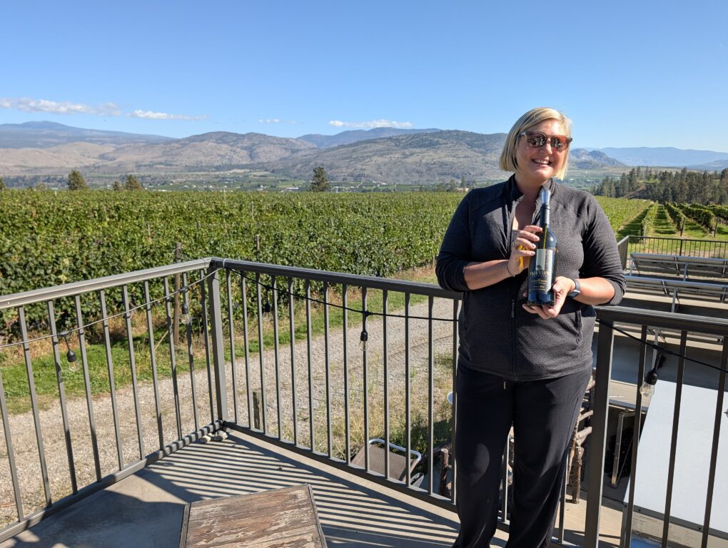 Osoyoos wine region winemaker Danielle Hutton shows off her a bottle of her wine while standing on a deck overlooking her vineyards