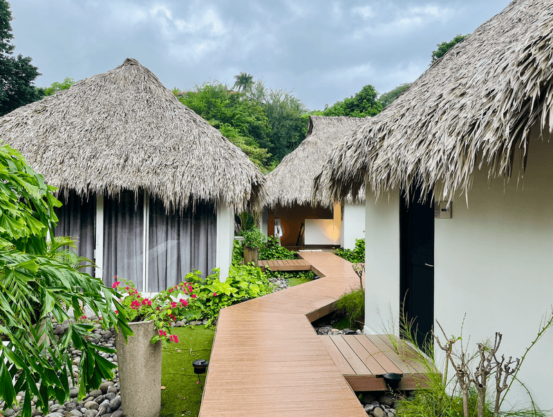 Three cabins with palapa roofs intersected by a wooden path