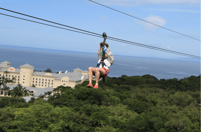 a woman ziplining above trees with an ocean view