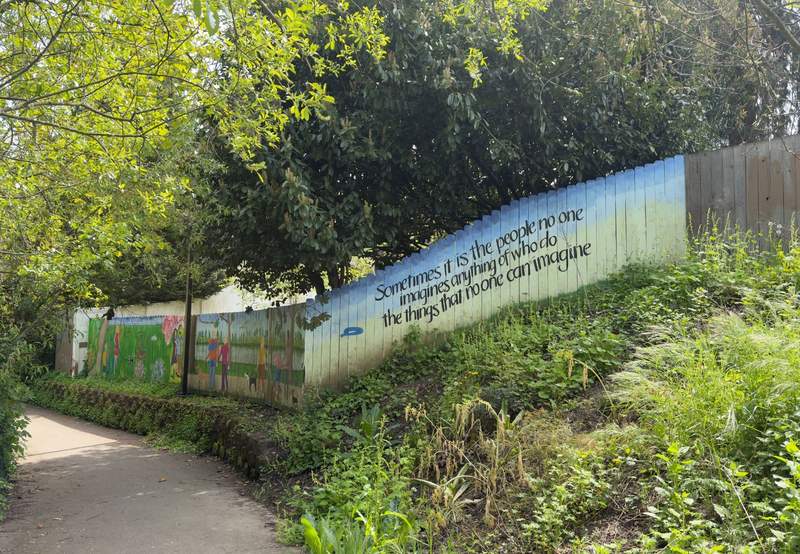 Painted fence with an inspirational quote along a tree lined walking path in Albany Oregon