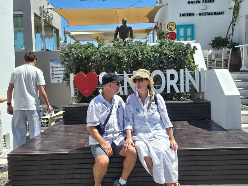 Couple sitting beneath the I Love Mykonos sign in Mykonos