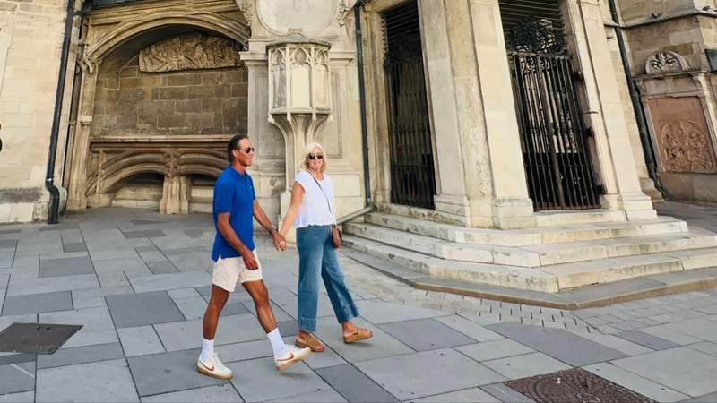 A couple walking hand in hand past an ornate historic church in Vienna, Austria.