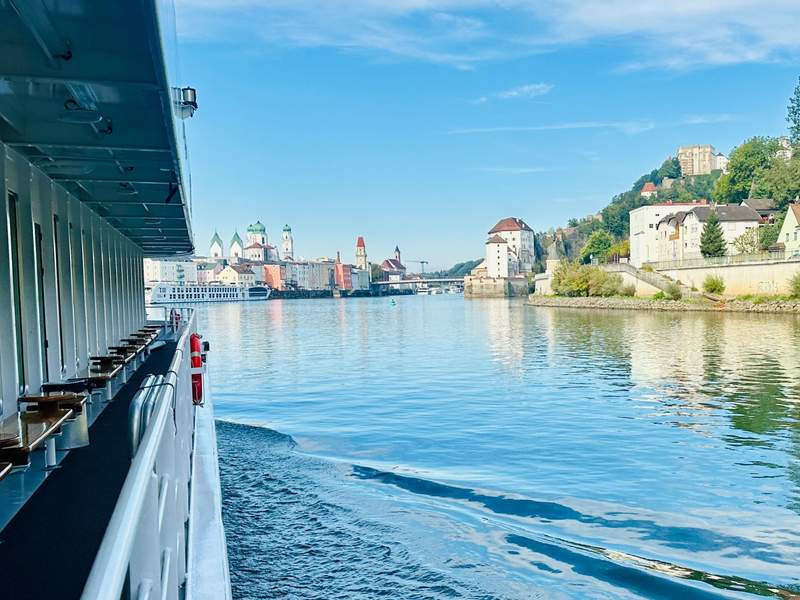 View from the MS Lisabelle as the riverboat sails past colorful buildings, church towers and a hillside in Passau, Germany.