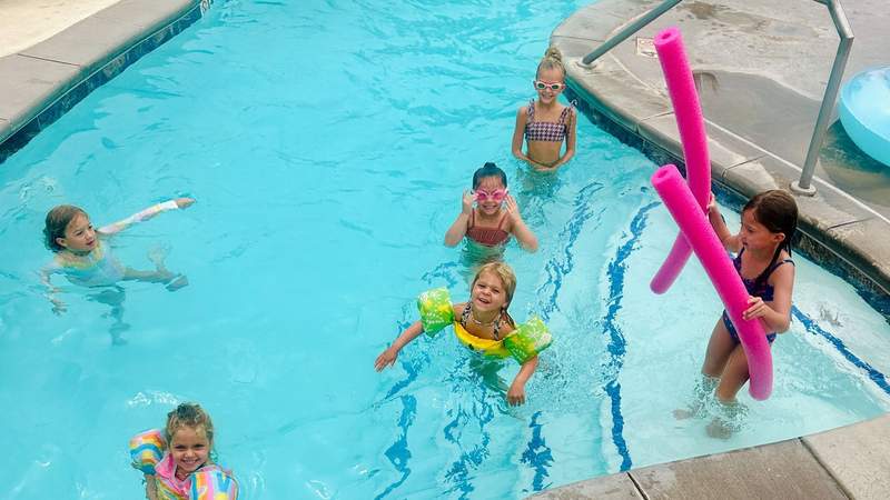 Six grandchildren swim and play with colorful pool noodles during a multigenerational family vacation.