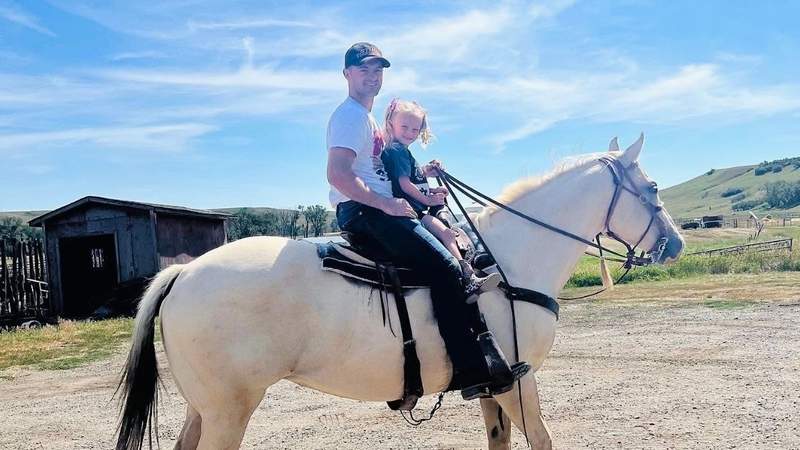 A man and his daughter ride a white horse together during a family ranch vacation.