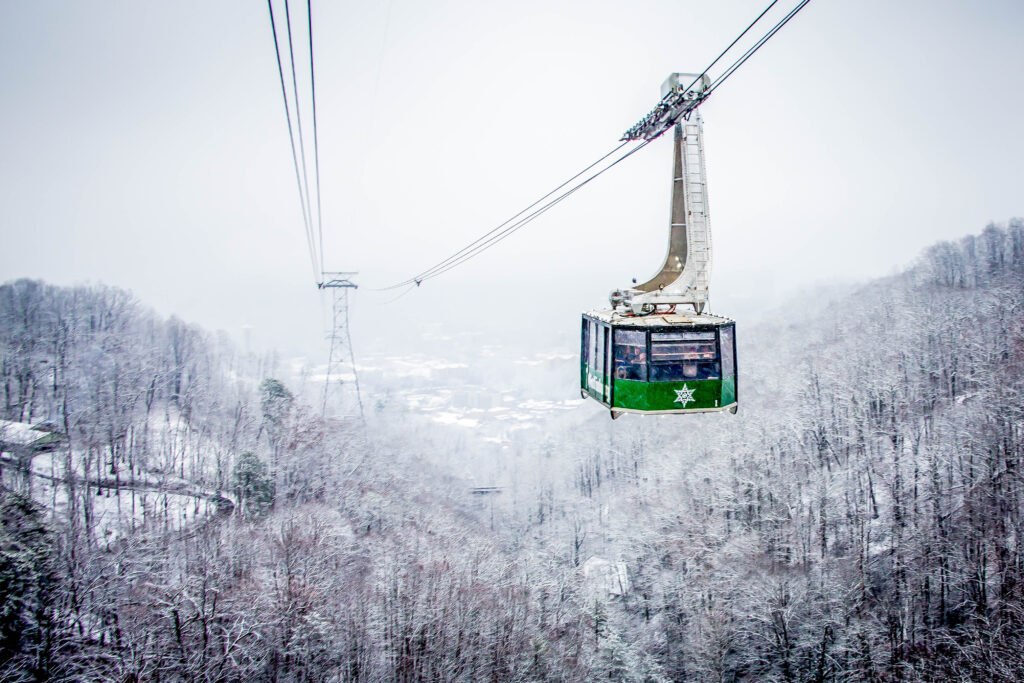 Green Ober Gatlinburg tram with winter snow-covered mountains in the background.