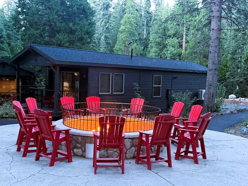 Circular outdoor fire pit with glowing flames surrounded by bright red Adirondack chairs at Waybound Yosemite.