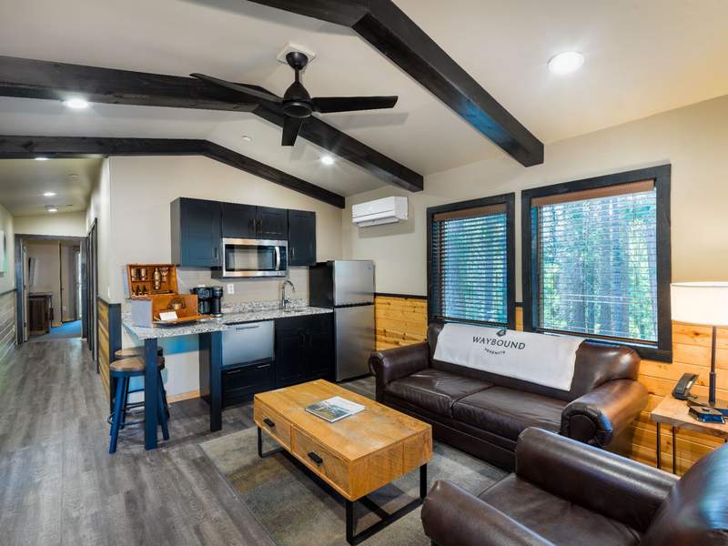 Interior of a Havens cabin at Waybound Yosemite featuring an open-concept living area with vaulted ceilings and exposed dark wood beams.