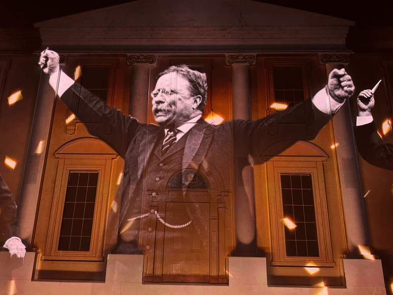 Theodore Roosevelt with his arms raised on a screen.