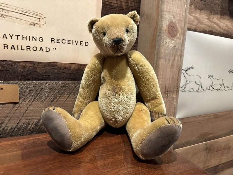 A tan colored teddy bear sitting on a shelf.