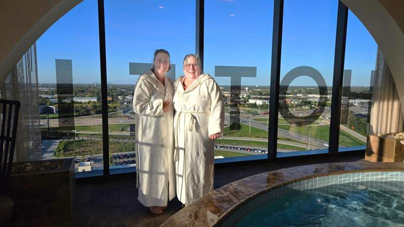 Two women in plush robes by the hot tub overlooking panoramic views at The Spa at Wind Creek Chicago Southland.