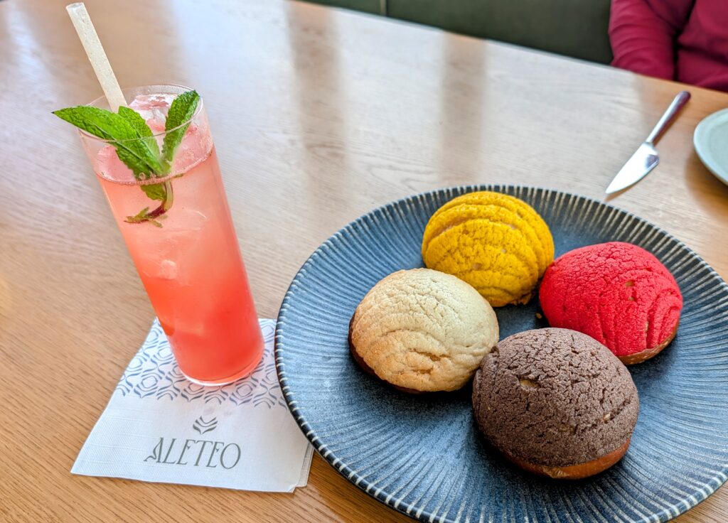 four colorful Conchas donuts -- one red, one yellow, one chocolate and one vanilla -- and a tall glass of pink drink, served at Aleto at The Monarch San Antonio hotel