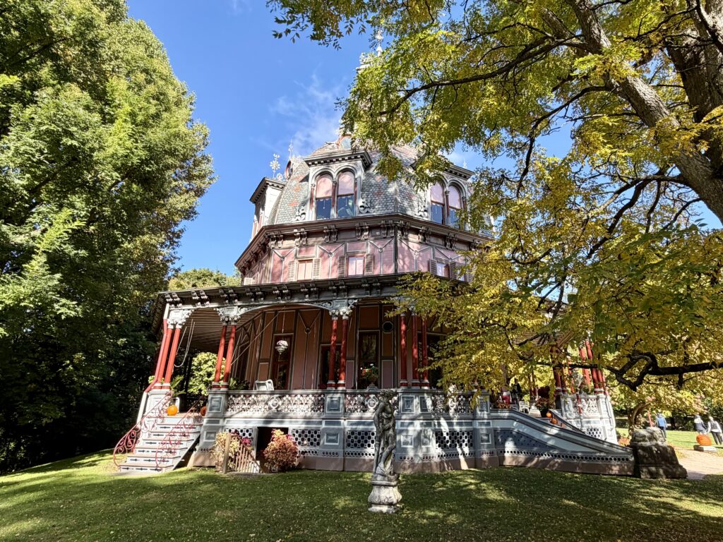 Pink Victorian octagon house framed by trees with Halloween pumpkins