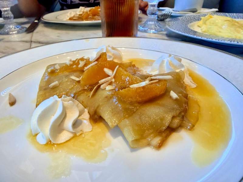 Crêpes Suzette served at Margaux restaurant in JW Marriott Grand Rapids, topped with orange slices, sliced almonds, Chantilly cream, and citrus sauce.