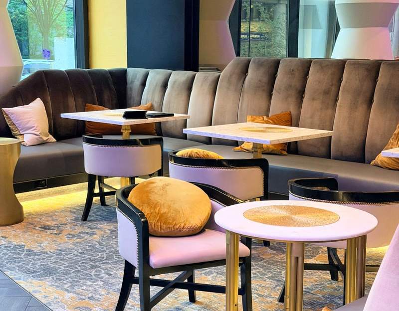 Stylish curved banquette seating, blush-colored chairs, marble-topped tables and gold accents at Rendezvous lobby bar inside Amway Grand Plaza.