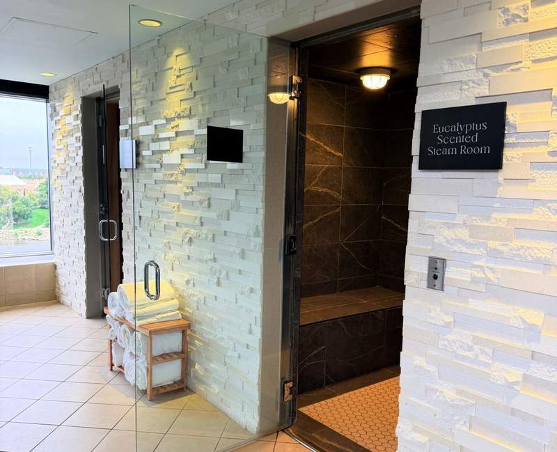Eucalyptus-scented steam room with dark stone walls, glass doors and neatly stacked white towels at the JW Marriott Grand Rapids spa.
