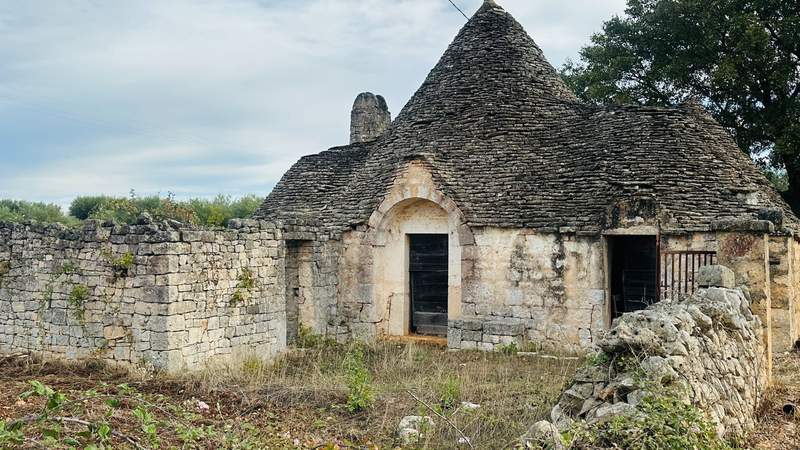 Rustic limestone trullo house with traditional cone-shaped stone roofs, weathered walls and wooden doors in the Puglia countryside of Italy.