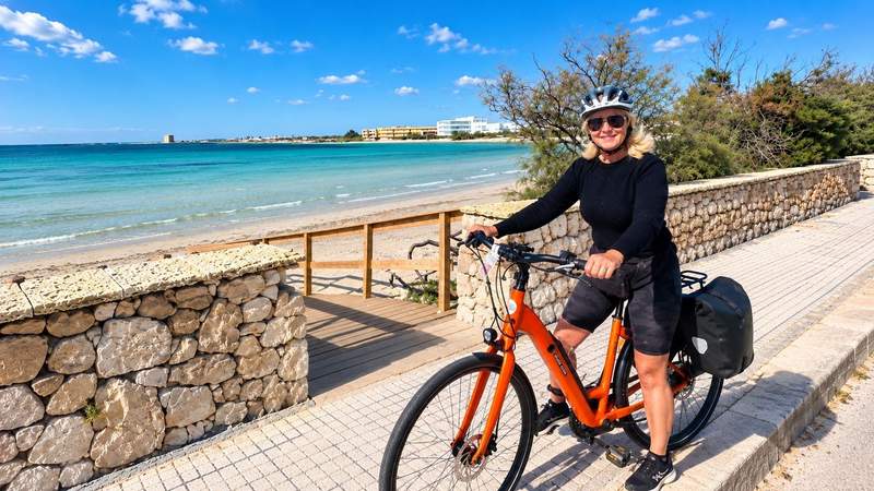 Woman wearing a cycling helmet poses with an orange e-bike beside a turquoise beach during a self-guided cycling tour through Puglia, Italy.