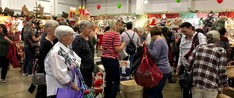 Women carrying tote bags browse a crowded indoor holiday boutique filled with Santa figures, nutcrackers and Christmas decorations